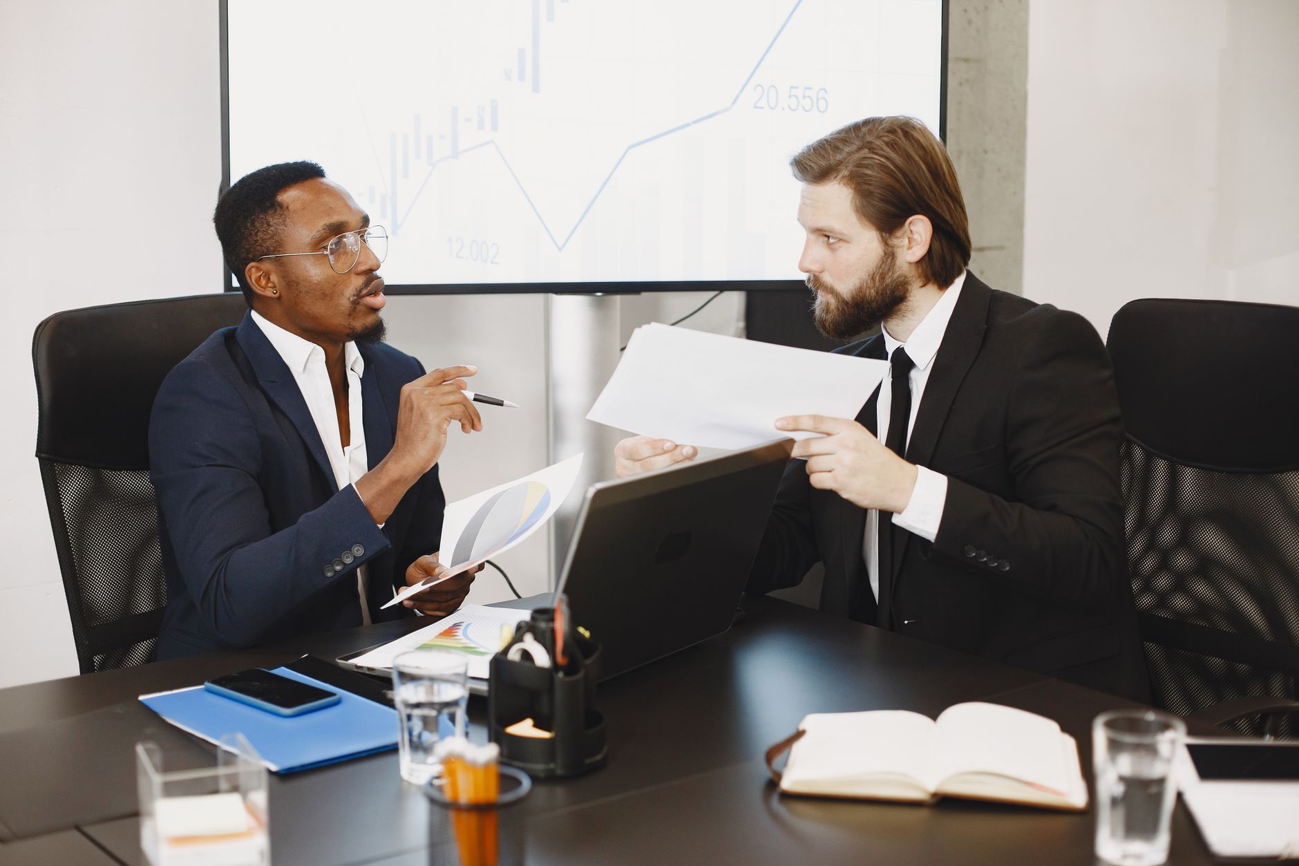 Two business professionals engaged in a planning meeting, discussing documents in a modern office setting. — Allergy Free Vin