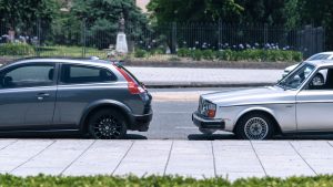 A close-up view of two cars parked on a city street near a green park on a sunny day. — Automotive Warranty Protects Primary