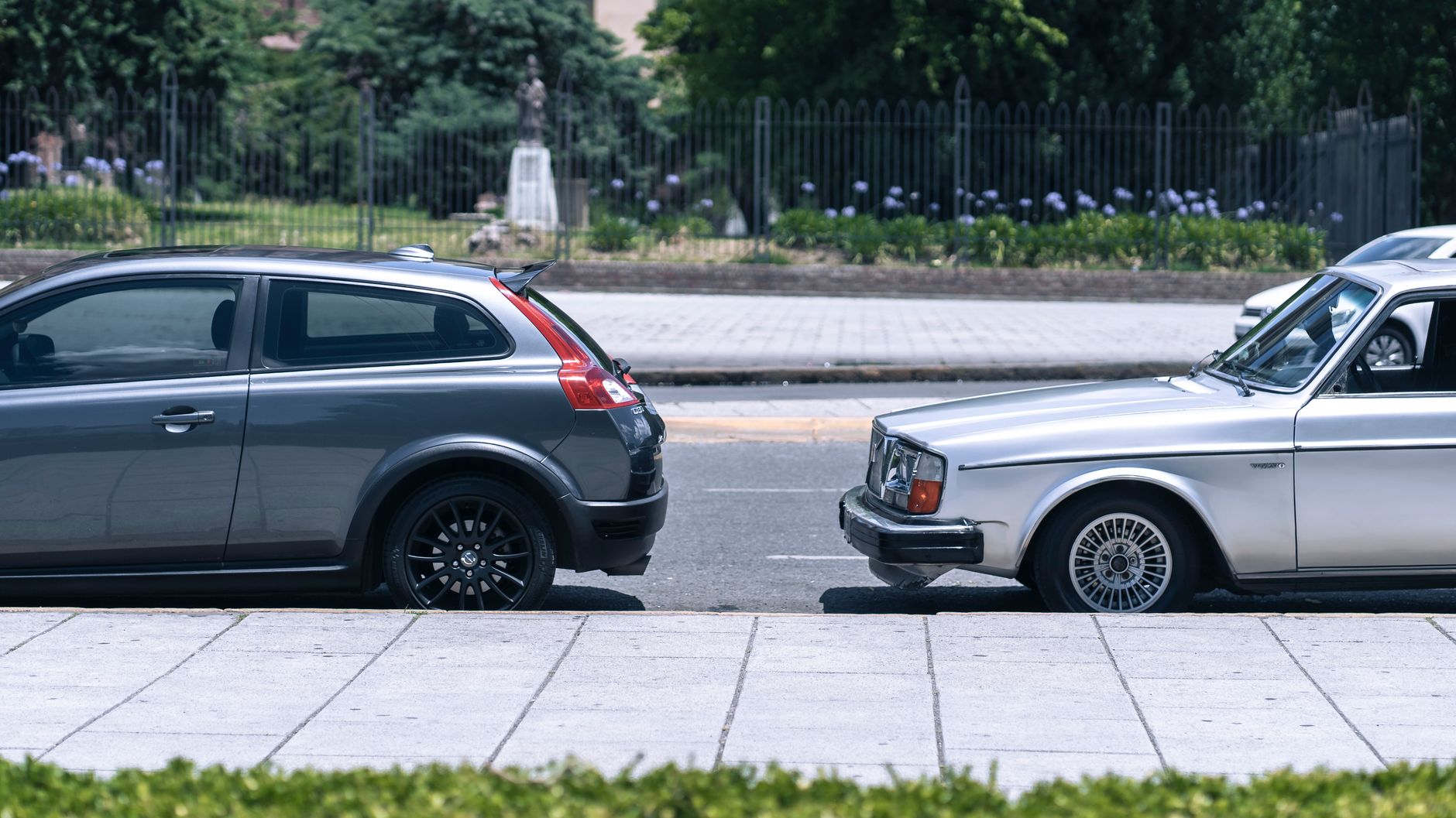 A close-up view of two cars parked on a city street near a green park on a sunny day. — Automotive Warranty Protects Primary