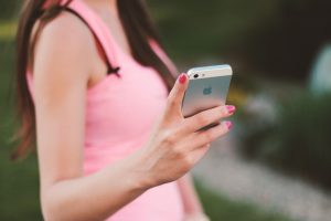 Close-up of a woman using a smartphone outdoors on a sunny day, wearing a pink tank top. — Boost Your Instagram Presence: Buy