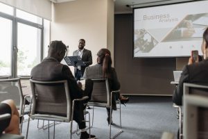 A business professional delivering a presentation in a conference room with diverse attendees. — Bulk Buying: The B2B Feature