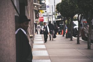 A man in a suit and hat leans against a city building, observing pedestrians. — Casting Calls and Curtain Calls: Tips for Fin