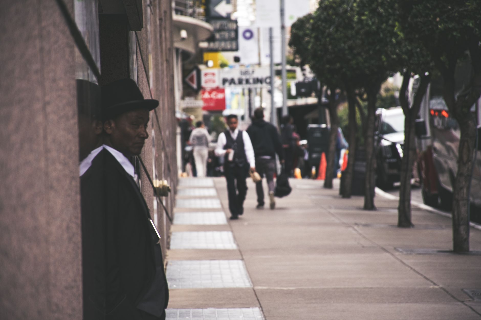 A man in a suit and hat leans against a city building, observing pedestrians. — Casting Calls and Curtain Calls: Tips for Fin