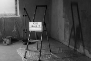 Black and white image of a step ladder with a 'home project' sign in a renovation setting. — Clear Lake Iowa Homes For Sale W