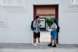 Two young travelers with backpacks share a moment at a cultural landmark, blending contemporary style with tradition. — Effec