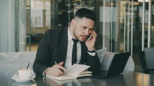 Businessman talks on phone while writing notes in a modern cafe. — Experiencing the Thrill of BuYiNs: A Must-Visit for Avid F