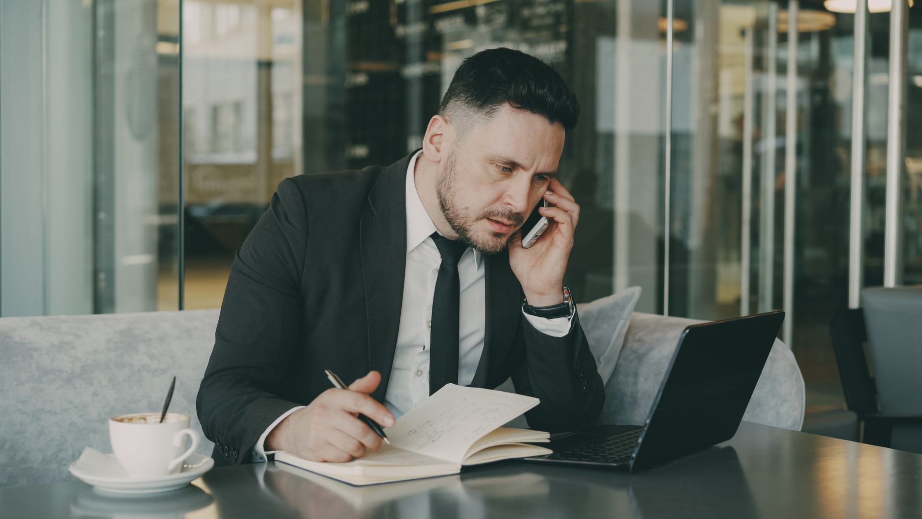 Businessman talks on phone while writing notes in a modern cafe. — Experiencing the Thrill of BuYiNs: A Must-Visit for Avid F