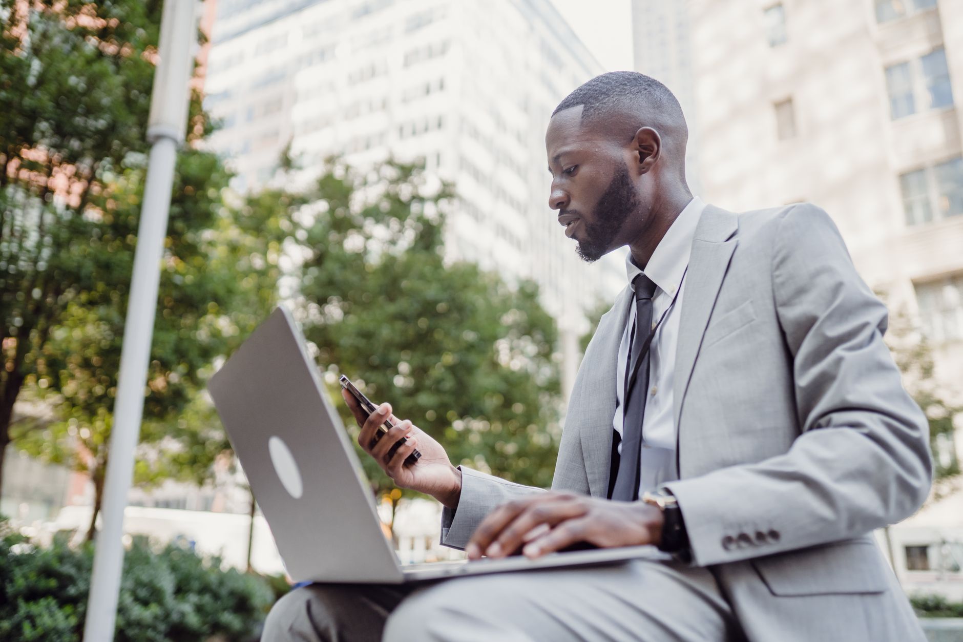 Businessman in a suit using a laptop and smartphone in an urban setting, blending technology with business. — From Seed to Do