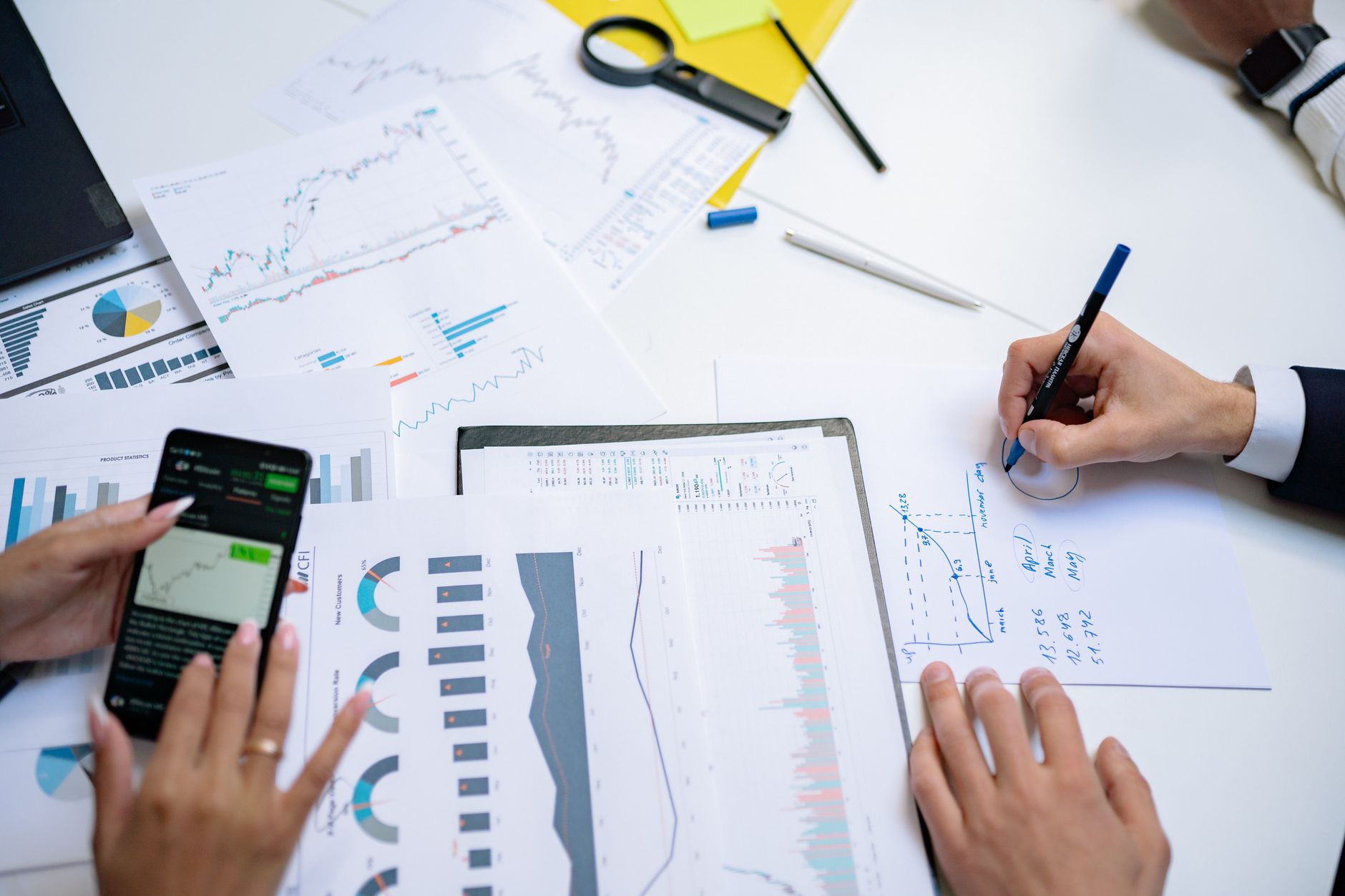 Colleagues collaborating on financial charts and graphs using mobile and paper documents in the office. — Get Expert Advice B