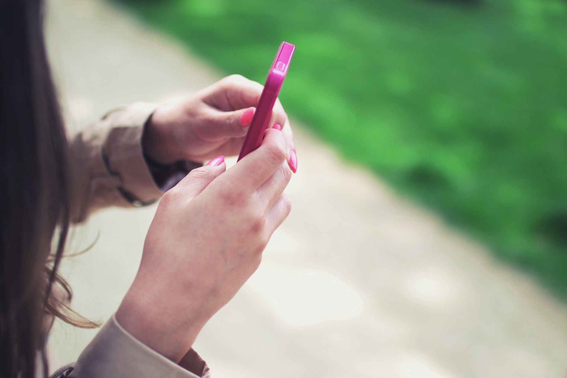 Woman holding a pink smartphone with both hands in a casual outdoor setting. — How Algorithms Can Manipulate Consumer Behavio