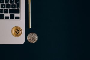 Close-up view of Bitcoin and Ethereum coins next to a laptop and pen on a black surface. — How Bitcoin Price Is Affected by E