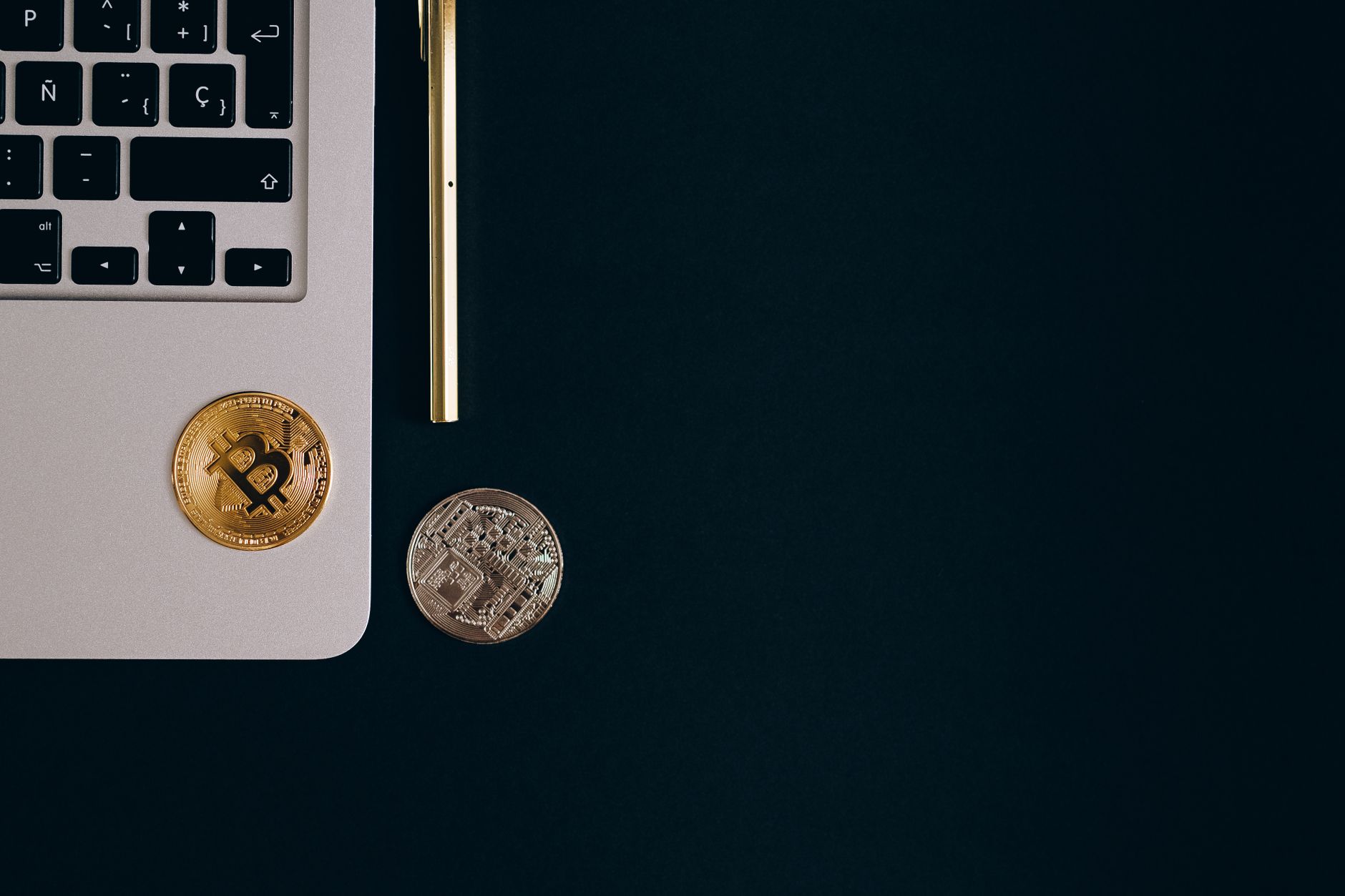 Close-up view of Bitcoin and Ethereum coins next to a laptop and pen on a black surface. — How Bitcoin Price Is Affected by E