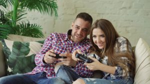 Happy couple enjoying video games together at home on a cozy sofa. — How Entertainment City Supports a Thriving Local Economy