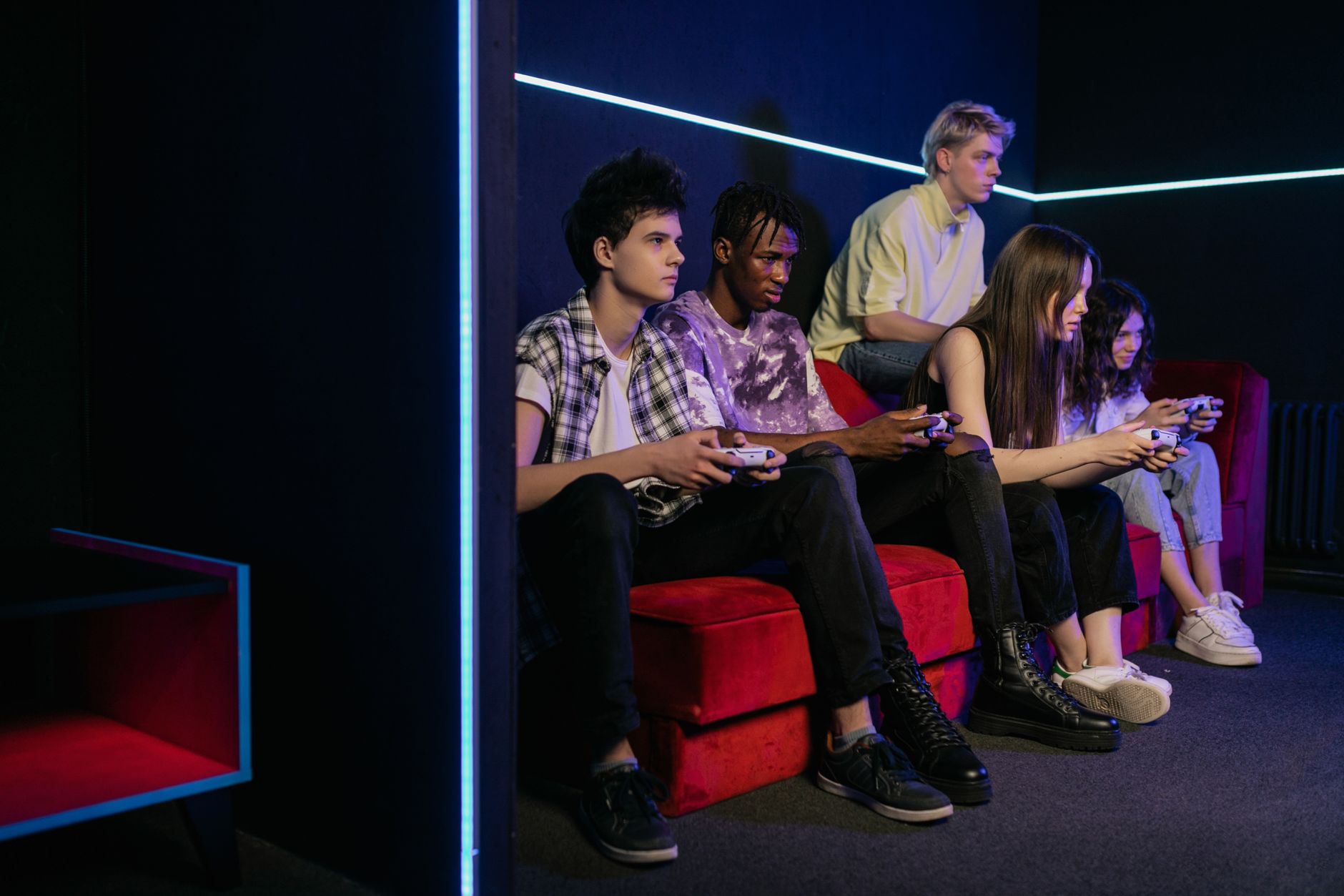 Teenagers enjoying video games together on a vibrant red couch in a modern gaming room. — Slots888 and the Benefits of Artifi