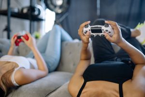 Two women relaxing and playing video games on a couch in a cozy living room. — Talking About PG