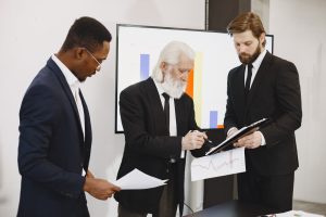 Three businessmen in suits reviewing reports and graphs during an office meeting. — The Best Dugouts for Any Baseball Team