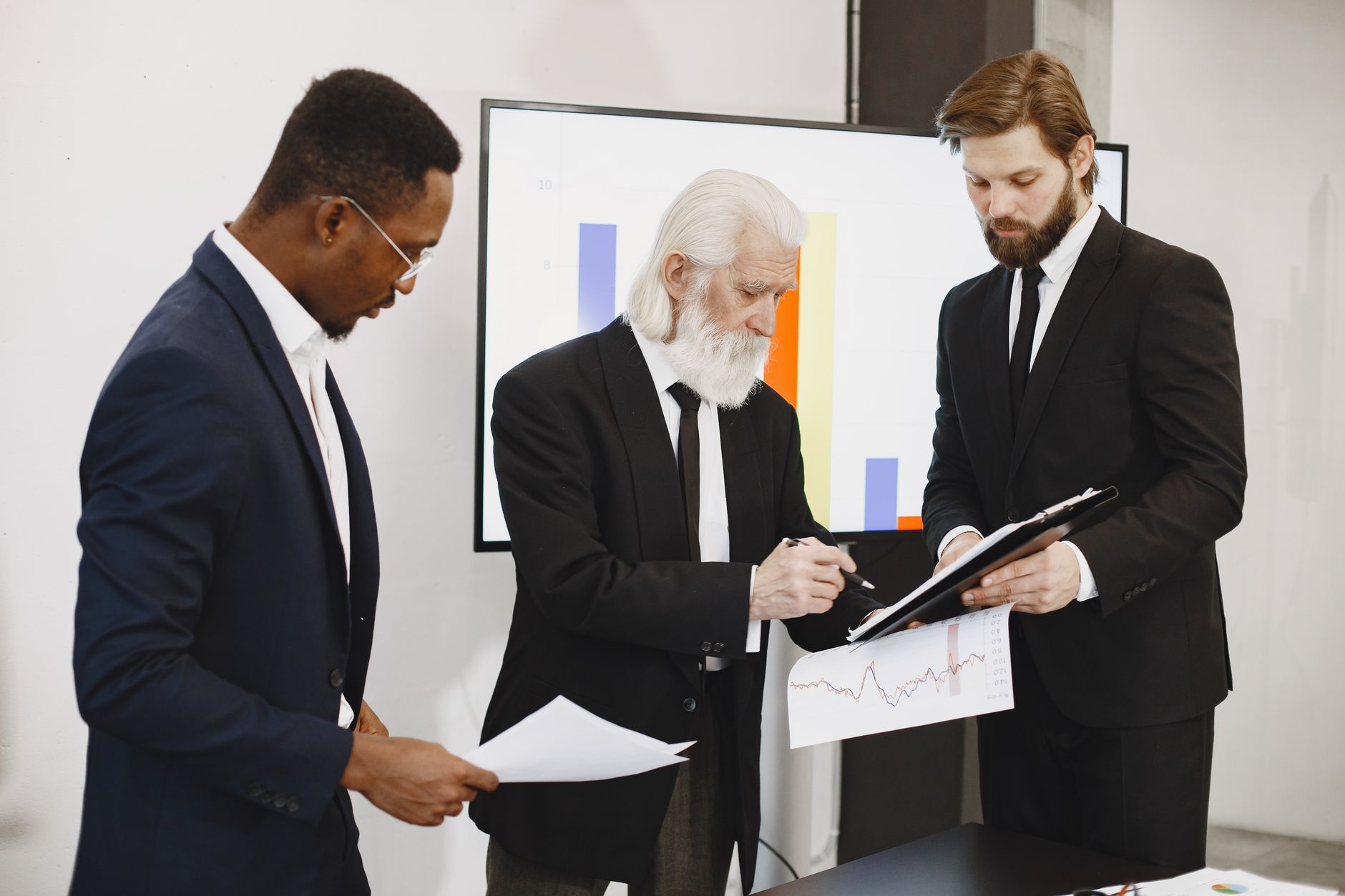 Three businessmen in suits reviewing reports and graphs during an office meeting. — The Best Dugouts for Any Baseball Team