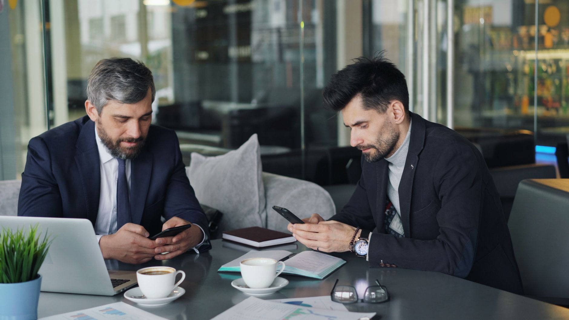 Two businessmen in a cafe working on smartphones and laptops, engaged in a meeting. — Types of White Label PPC services and P