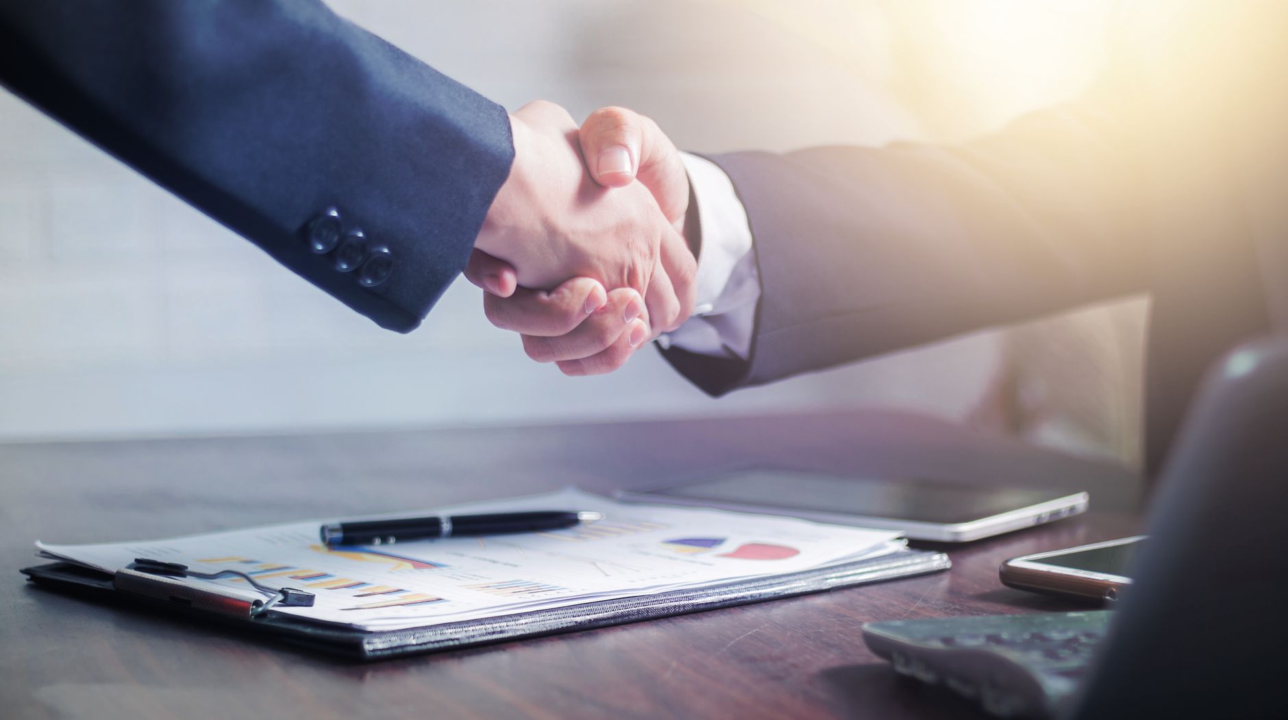 Professional handshake agreement over business charts in an office setting. — Unlocking Your Inner Passion Through Tantric Ma