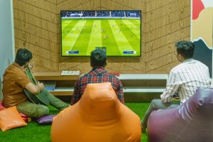 Three friends relaxing and playing a soccer video game indoors on a comfortable game night. — Why Is It Beneficial to Play Ca