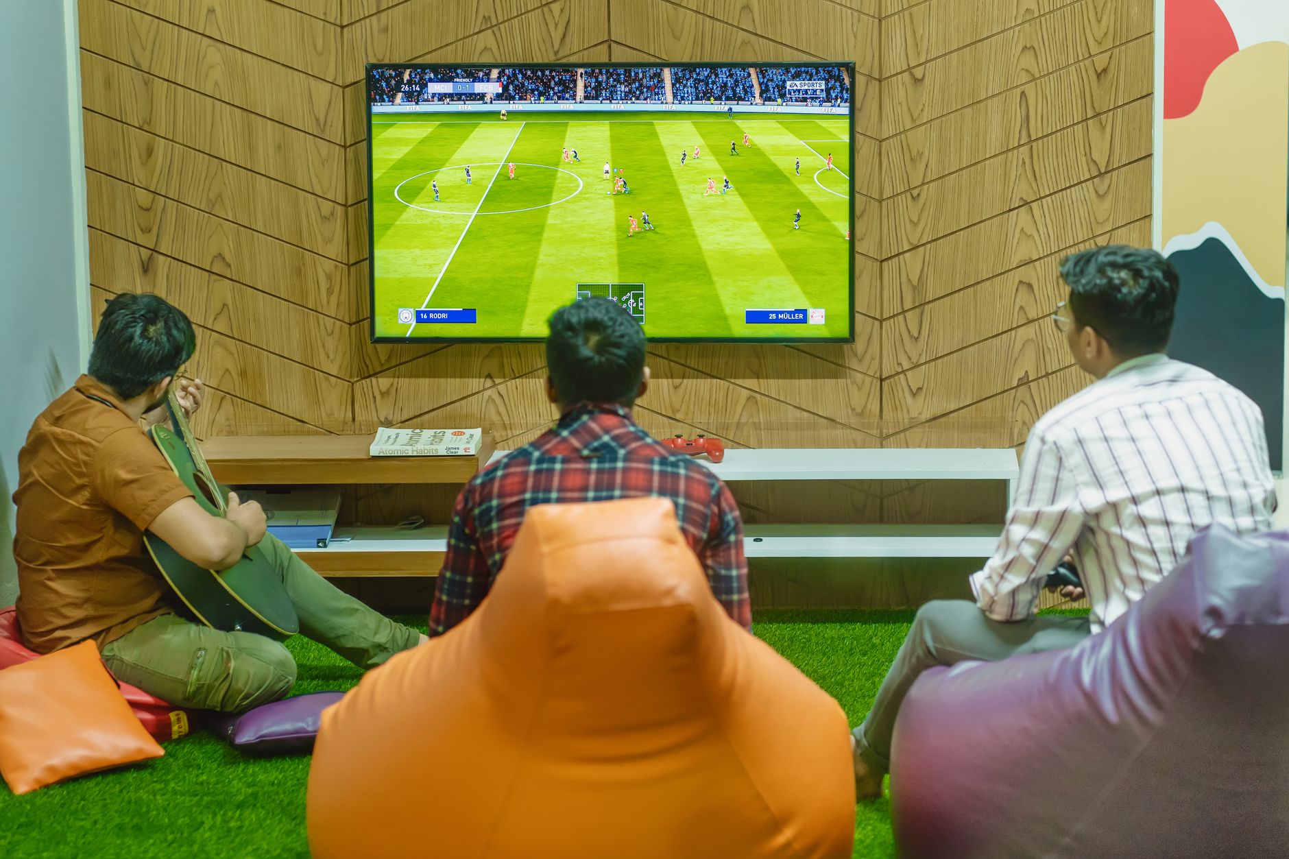 Three friends relaxing and playing a soccer video game indoors on a comfortable game night. — Why Is It Beneficial to Play Ca